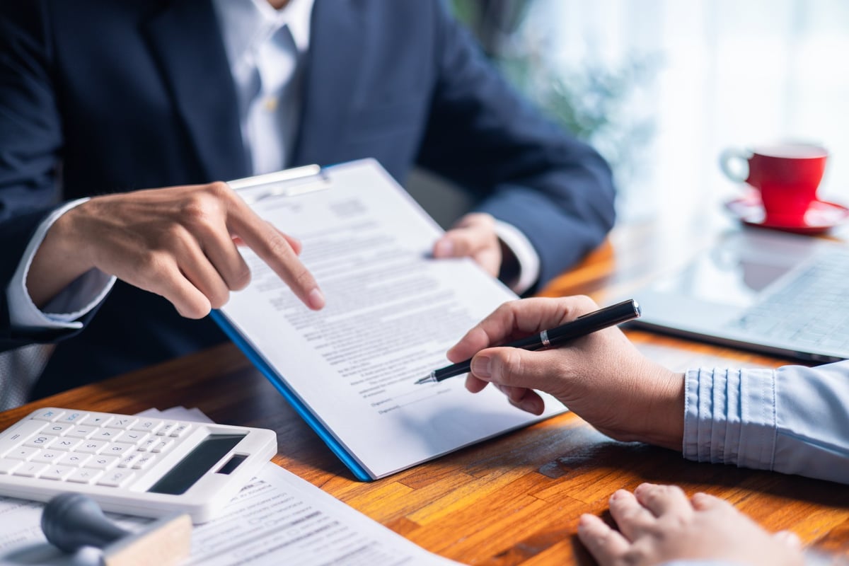 Businesswoman reviewing mortgage document and contract with a client at a desk