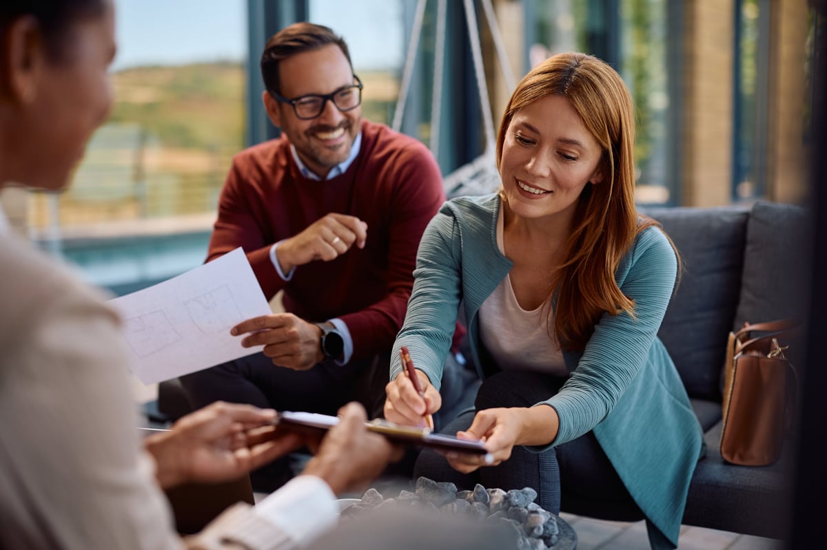 Happy woman signing an agreement with insurance agent while buying new house with her husband.