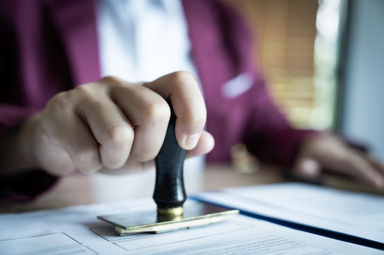 A person is stamping a document with a stamp, the stamp is black and gold, the person is wearing a red jacket
